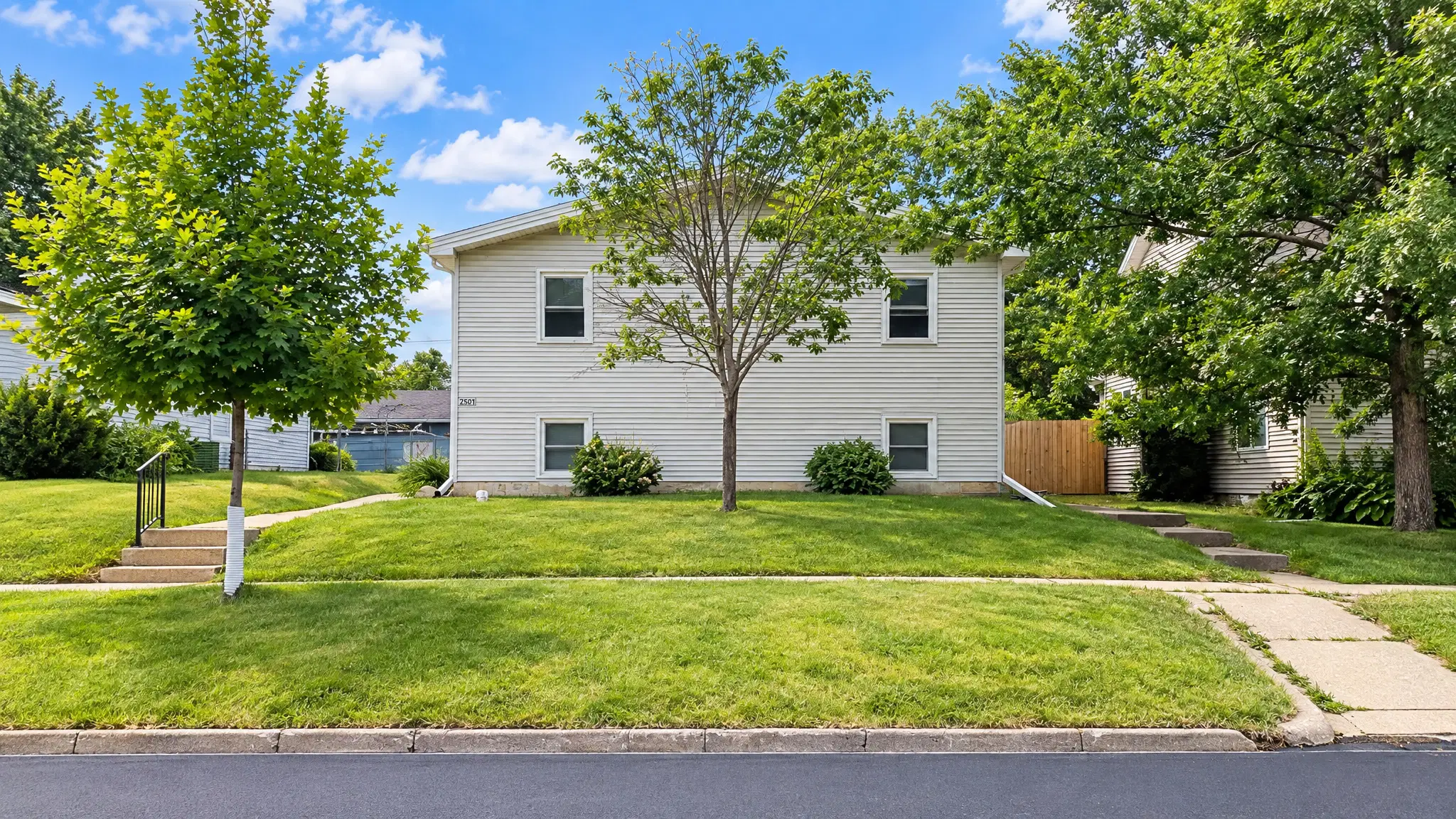White and pale-grey two-storey rental home with dark-framed windows, green lawn and mature trees
